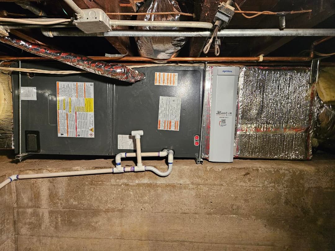 Basement HVAC system with insulated ducts and warning labels on the unit.