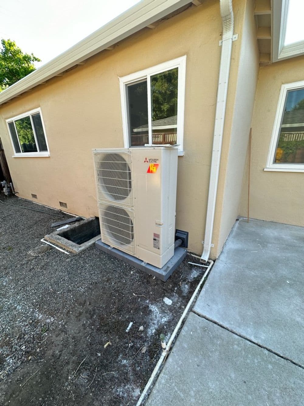 Mitsubishi air conditioning unit installed outside a beige house next to a concrete walkway.