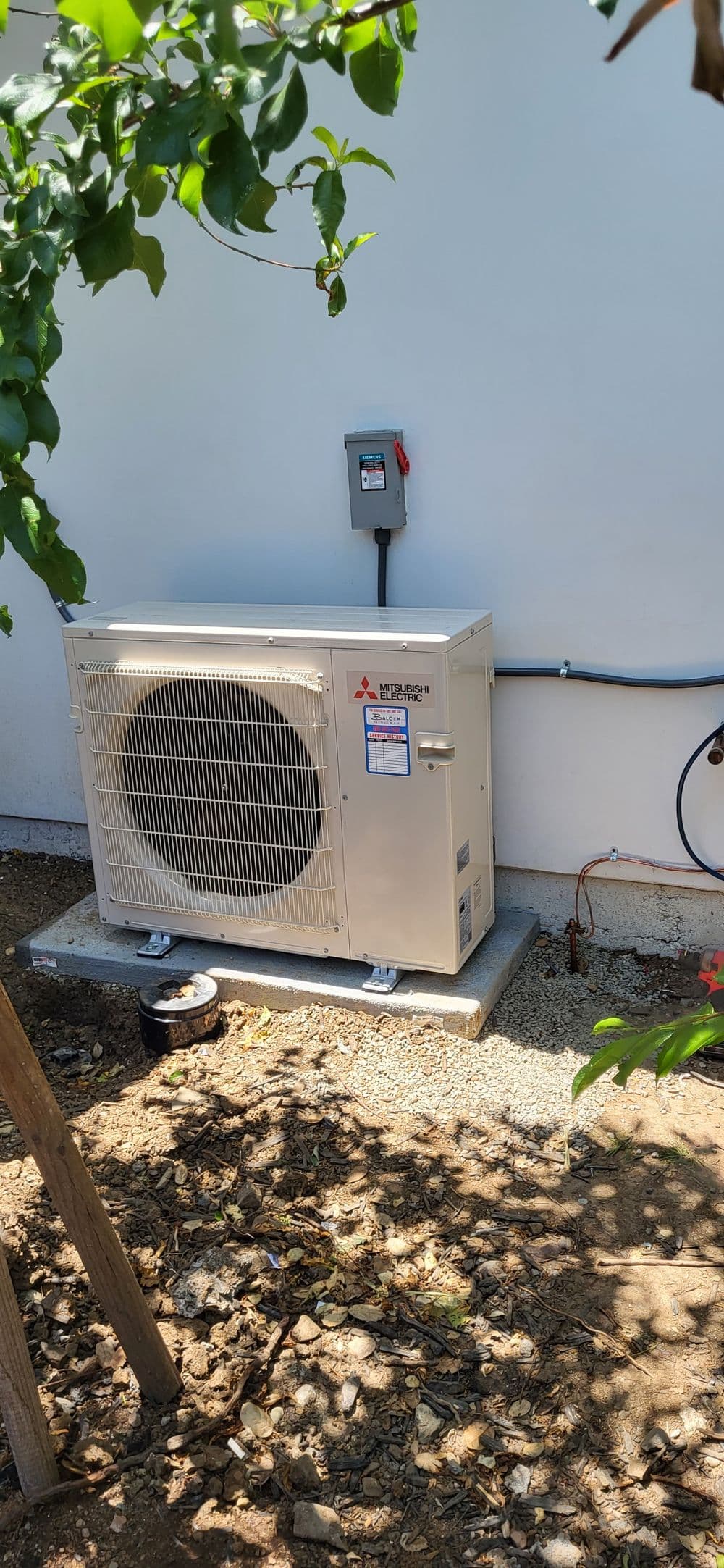 Mitsubishi outdoor heat pump unit installed next to a building, surrounded by greenery.