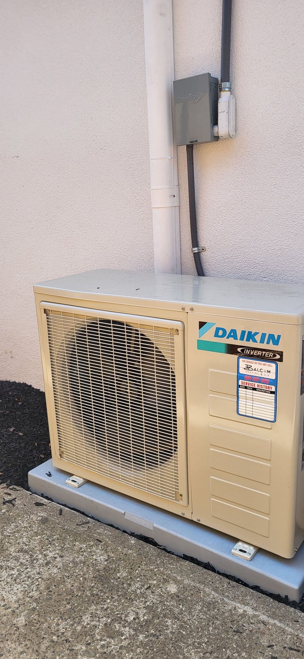 Daikin inverter air conditioning unit mounted outside a building on a concrete base.