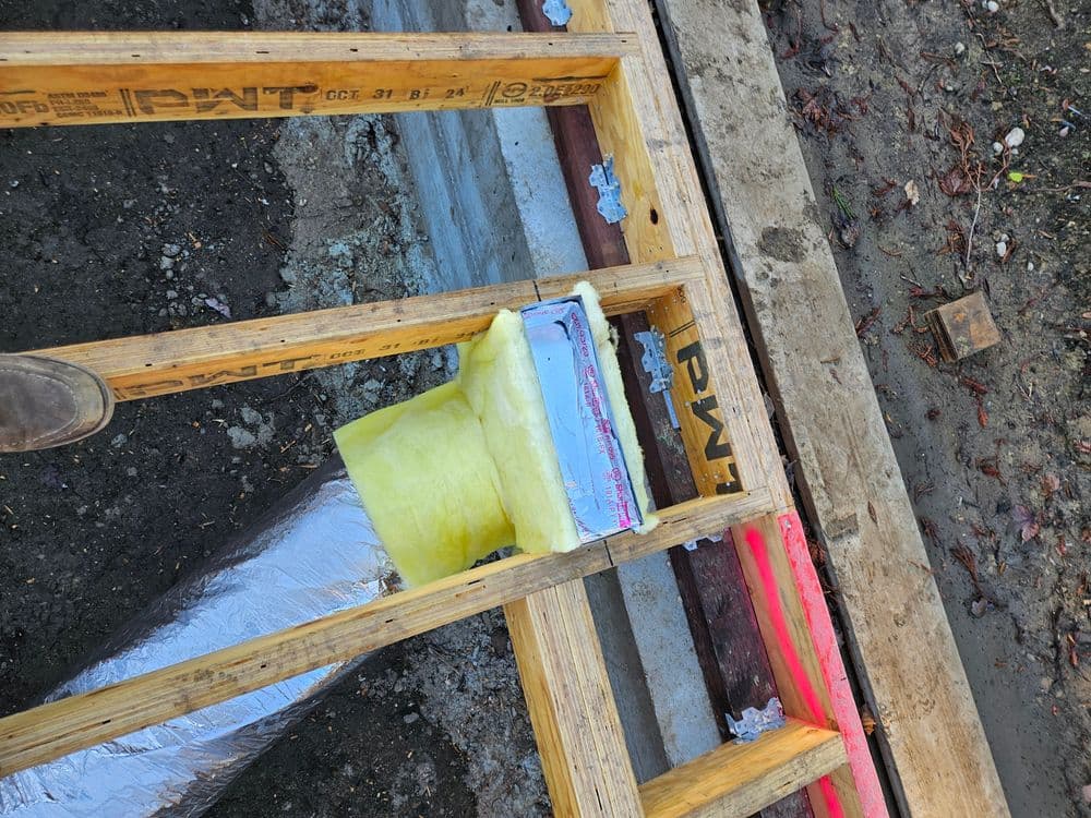 Construction site showing wood framing with insulation and plumbing details.