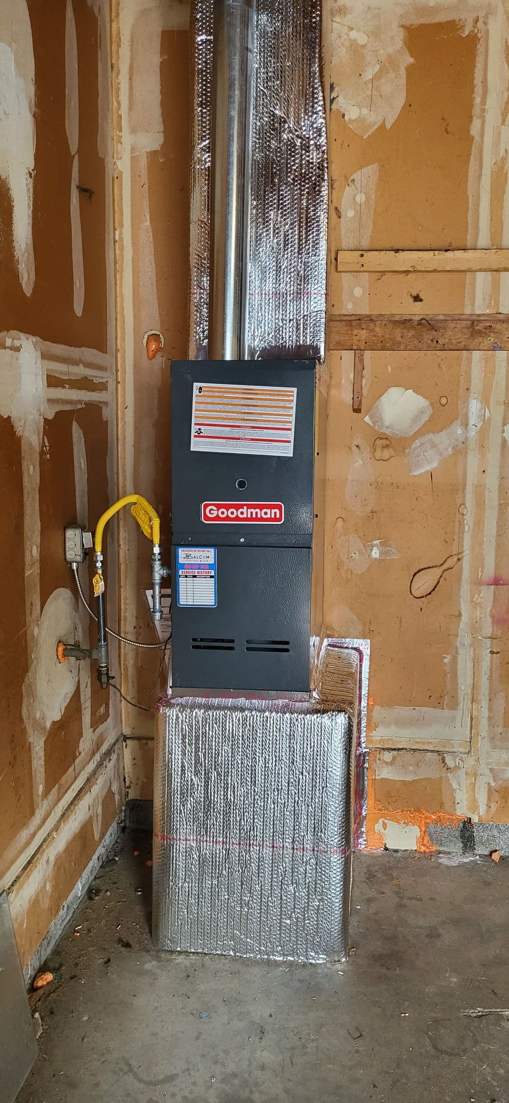 Goodman furnace installed in a garage, with insulated pipes and surrounding wall details.