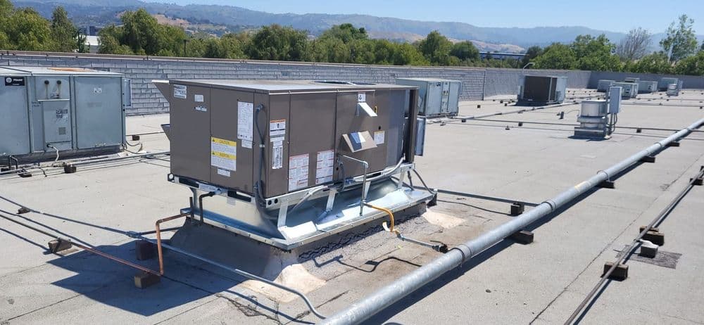 Rooftop HVAC unit with ductwork and ventilation systems against a clear blue sky.