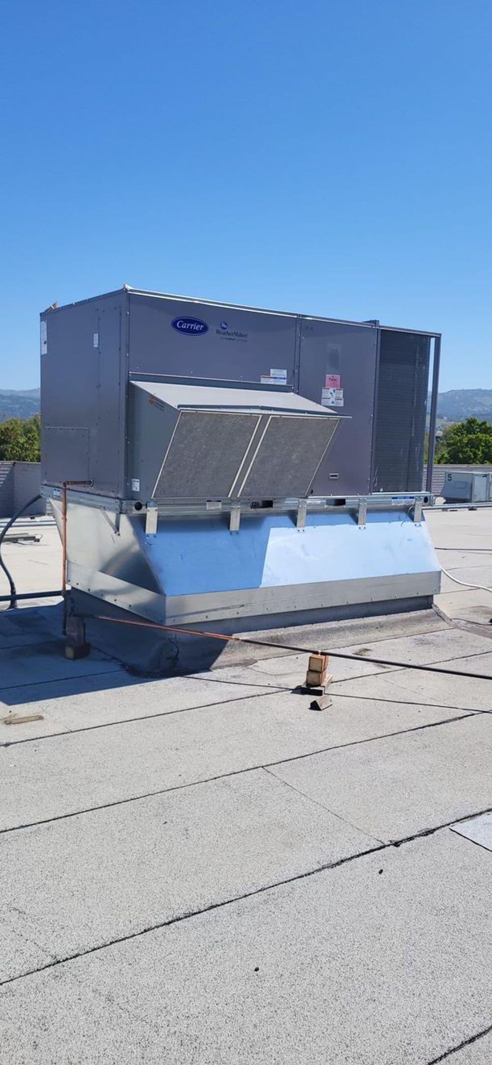 Commercial rooftop HVAC unit on a flat roof against a clear blue sky.